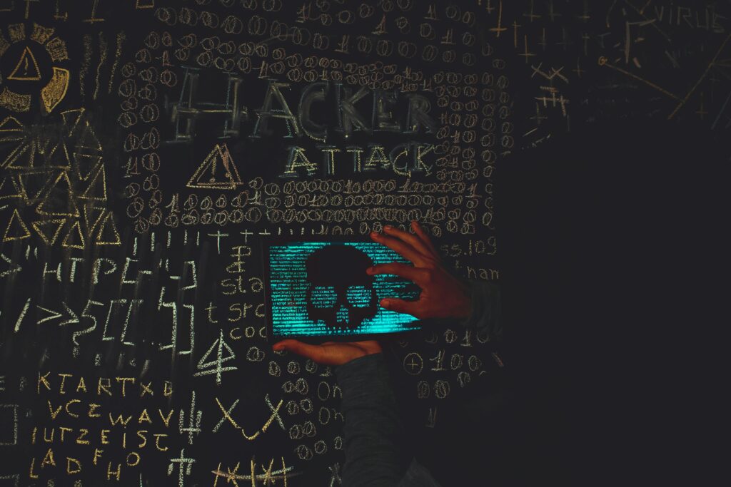 A hacker in a black hoodie using a tablet displaying a skull, surrounded by chalk symbols and'Hacker Attack' text.